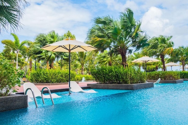 A swimming pool with palm trees and umbrellas. - Timurbay Seafront Apartment by My Seasons (Kuantan)