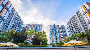 A high-rise residential building with multiple balconies, surrounded by palm trees and a paved walkway. - Timurbay Seafront Apartment by My Seasons (Kuantan)