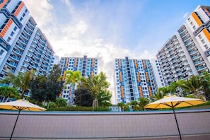 Un edificio residencial alto con varios balcones, rodeado de palmeras y un sendero pavimentado.