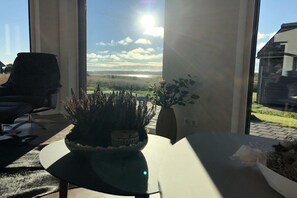 A modern interior with a view of a landscape through large windows, a round table, and a chair. - Painters' Corner Hohwacht (Hohwacht)
