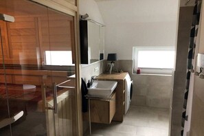A compact bathroom with a glass shower enclosure, a sink, a mirror, and a window. - Painters' Corner Hohwacht (Hohwacht)