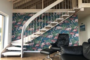 Un intérieur moderne avec un escalier, un fauteuil en cuir noir et un mur orné d’un motif de flamants roses.