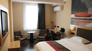 Une chambre d’hôtel avec un lit, un bureau, deux chaises, une petite table, un téléviseur et une fenêtre avec des rideaux.