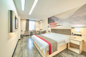 Habitación de hotel con una cama grande, un escritorio, una silla, una mesita y un cuadro de un paisaje montañoso.