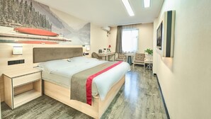Une chambre d’hôtel comprenant un lit, un bureau, une chaise, une petite table, un téléviseur fixé au mur et une fenêtre avec des rideaux.