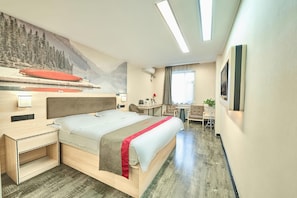Hotellihuone, jossa on sänky, työpöytä, tuoli, pieni pöytä, seinälle asennettu televisio ja ikkuna, jossa on verhot.