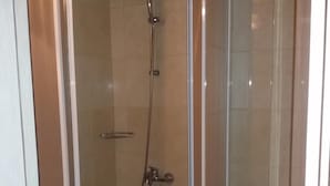 Cabina de ducha con paredes de vidrio, cabezal de ducha de mano y grifo instalado en la pared.