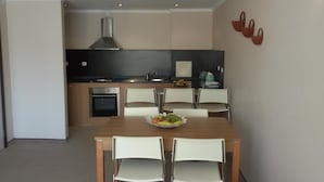 Una cocina moderna con horno integrado, estufa y campana extractora. Hay una mesa de comedor con cuatro sillas y un frutero encima.