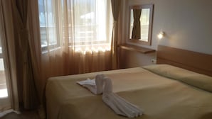 Una habitación de hotel con cama, cortinas, un espejo y una ventana.