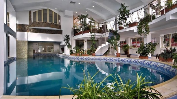 Una piscina interior con una escalera central, rodeada de balcones con plantas en macetas.