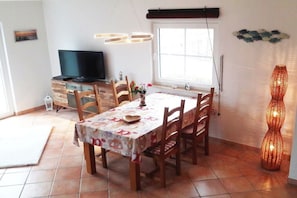 A dining area with a table set for four, a television on a cabinet, and a decorative vase on the table. - Holiday home in Rügen with 2 bedrooms (Putgarten auf Rügen)