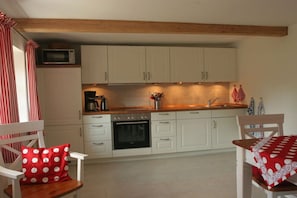 A compact kitchen with white cabinets, a microwave, a coffee maker, and a sink. There are two chairs with red and white polka dot cushions. - Holiday home with 3 bedrooms (Vollerwiek)