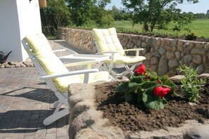 A patio with two white lounge chairs and a stone wall. - Holiday home with 3 bedrooms (Vollerwiek)