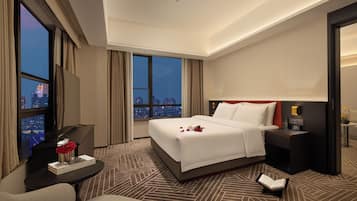 Habitación de hotel con una cama grande, un escritorio con una computadora, una silla y vistas a la ciudad a través de las ventanas.