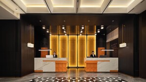 Ein Hotel-Empfangsbereich mit modernem Design, ausgestattet mit einem Marmor-Empfangstresen, einer Rezeption und einem gemusterten Boden.