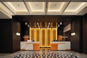 Un espace d’accueil d’hôtel au design moderne, comprenant un comptoir de réception en marbre, un guichet d’enregistrement et un sol à motifs.