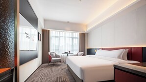 Ein Hotelzimmer mit Bett, Schreibtisch, zwei Stühlen, einem Vorhangfenster und einem gemusterten Teppich.