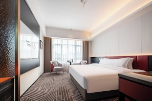 Une chambre d’hôtel avec un lit, un bureau, deux chaises, une fenêtre avec des rideaux et une moquette à motifs.