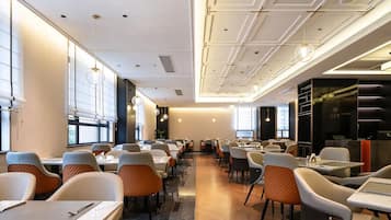 Un comedor moderno con mesas y sillas, ventanas amplias e iluminación empotrada en el techo.