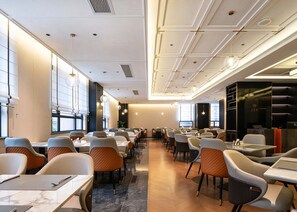Un comedor moderno con mesas y sillas, ventanas amplias e iluminación empotrada en el techo.