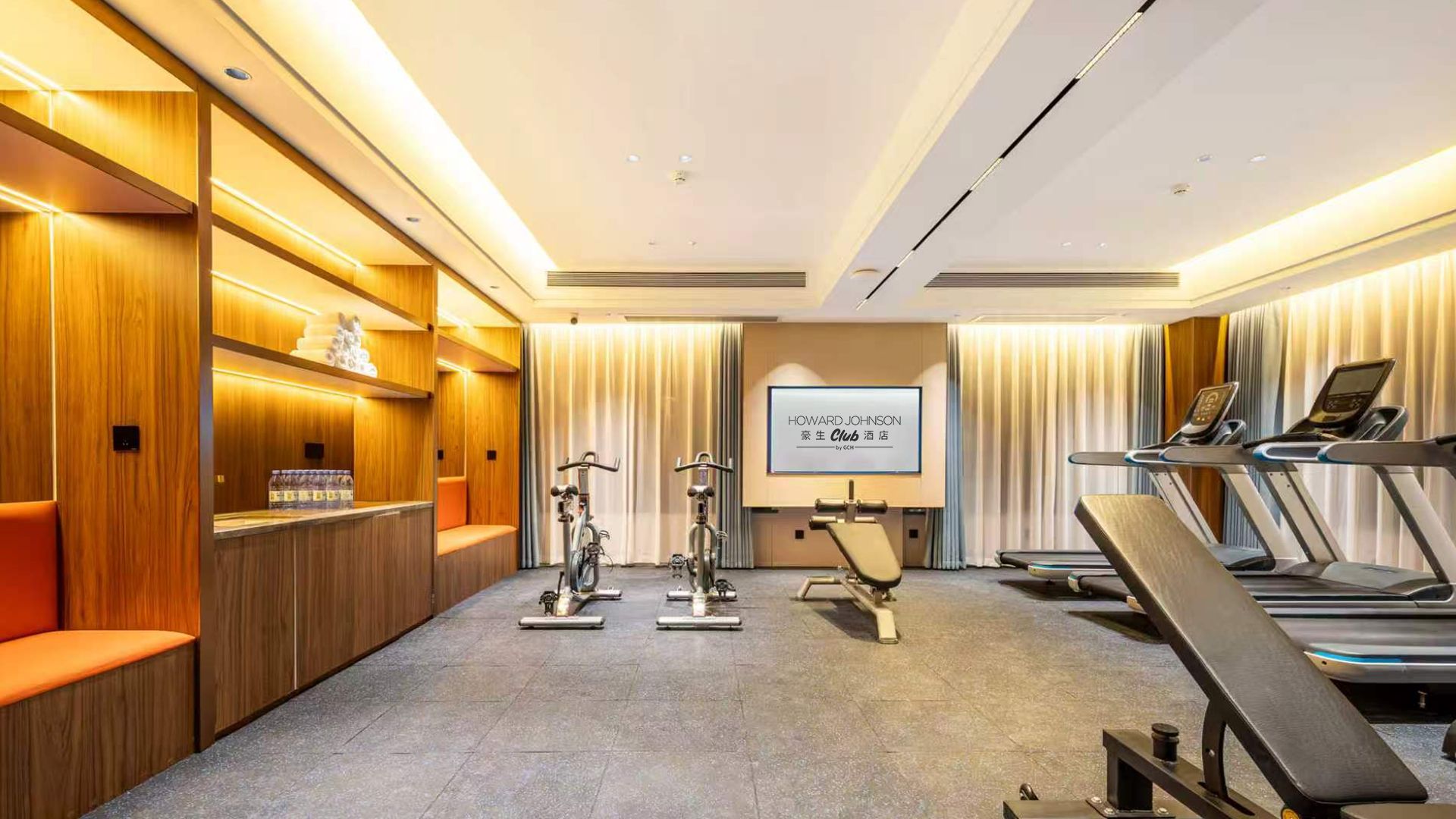 Un gimnasio de hotel con equipo de ejercicio, una pantalla de proyección y una zona de estar.