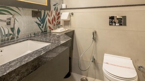 A bathroom with a large mirror, a sink, a toilet, and a shower. - Hotel Highway King (Jaipur)