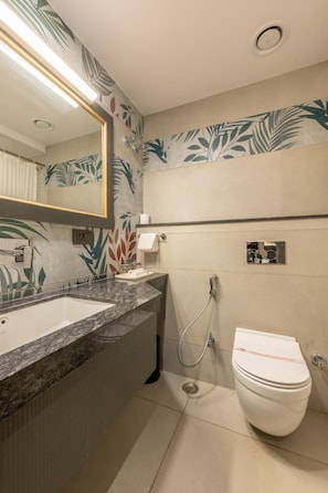 A bathroom with a large mirror, a sink, a toilet, and a shower. - Hotel Highway King (Jaipur)