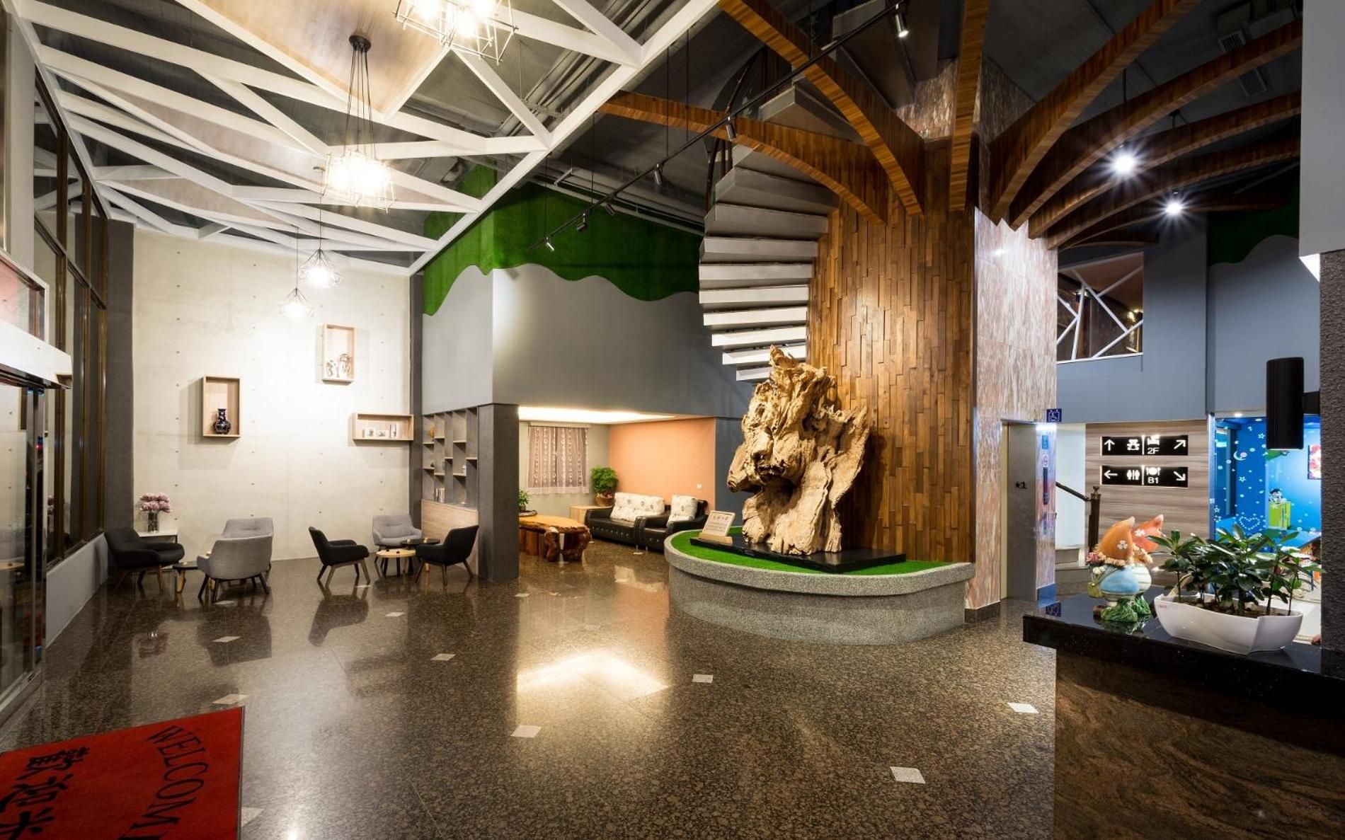 A modern lobby with a central wooden sculpture, seating area, and directional signs.