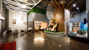 A modern lobby with a central wooden sculpture, seating area, and directional signs. - Yadi Hotel (Puli)