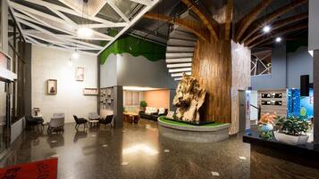 A modern lobby with a central wooden sculpture, seating area, and directional signs.
