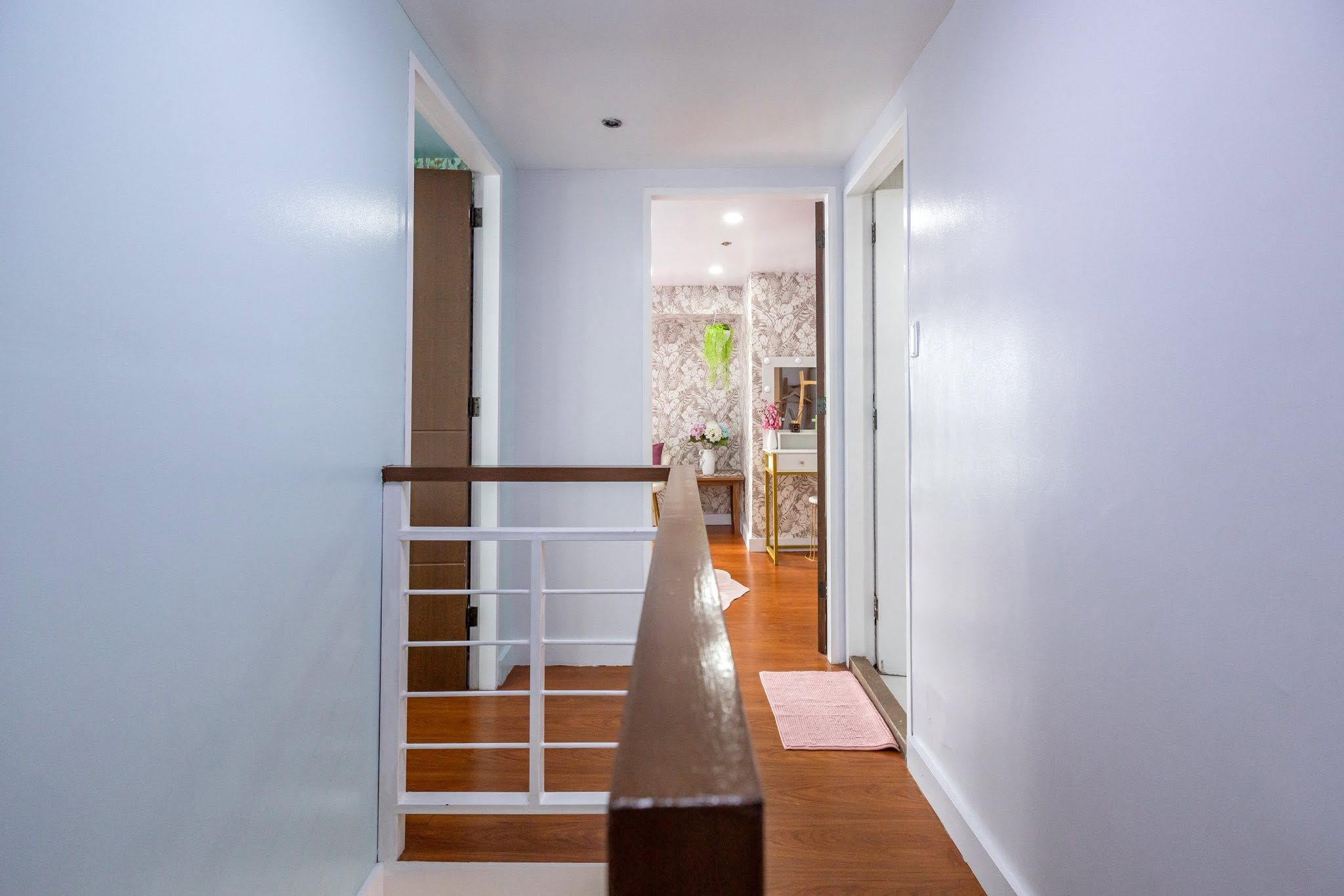 A hallway with a wooden staircase, a small table with a vase of flowers, and a mirror on the wall.