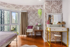 A modern bedroom with a large window, a vanity with a mirror, and a small table with a vase of flowers. - Spacious 2BR BGC Stay City View Fort Victoria Family & Group Friendly Stay (Taguig)