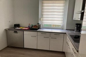 A modern kitchen with a dishwasher, a coffee maker, and a window with blinds. - Holiday apartment with 4 bedrooms (Lübbenau)
