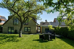 A residential property with a well-maintained lawn, a dining area with outdoor furniture, and a brick house with a tiled roof. - House Sorgenfrei Holiday Home No. 7 (Travemünde)