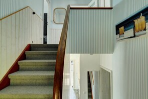 A staircase with wooden handrails and carpeted steps leading to a room with striped wallpaper and a framed picture of beach chairs. - House Sorgenfrei Holiday Home No. 7 (Travemünde)