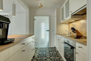 Une cuisine avec des meubles blancs, une machine à café, un évier et des carreaux de sol à motifs.