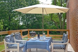 Ein Essbereich im Freien mit einem Tisch für zwei Personen, einem Grill und einem großen Sonnenschirm, der Schatten spendet.