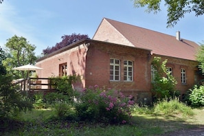 Ein Gebäude aus Backsteinen mit einem geneigten Dach, einem Holzzaun und einem Garten mit verschiedenen Pflanzen und Blumen.