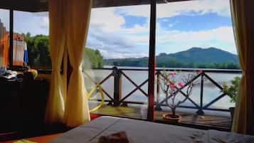A room with a bed, curtains, and a view of a lake and mountains.
