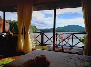 Quarto com cama, cortinas e vista para um lago e montanhas.