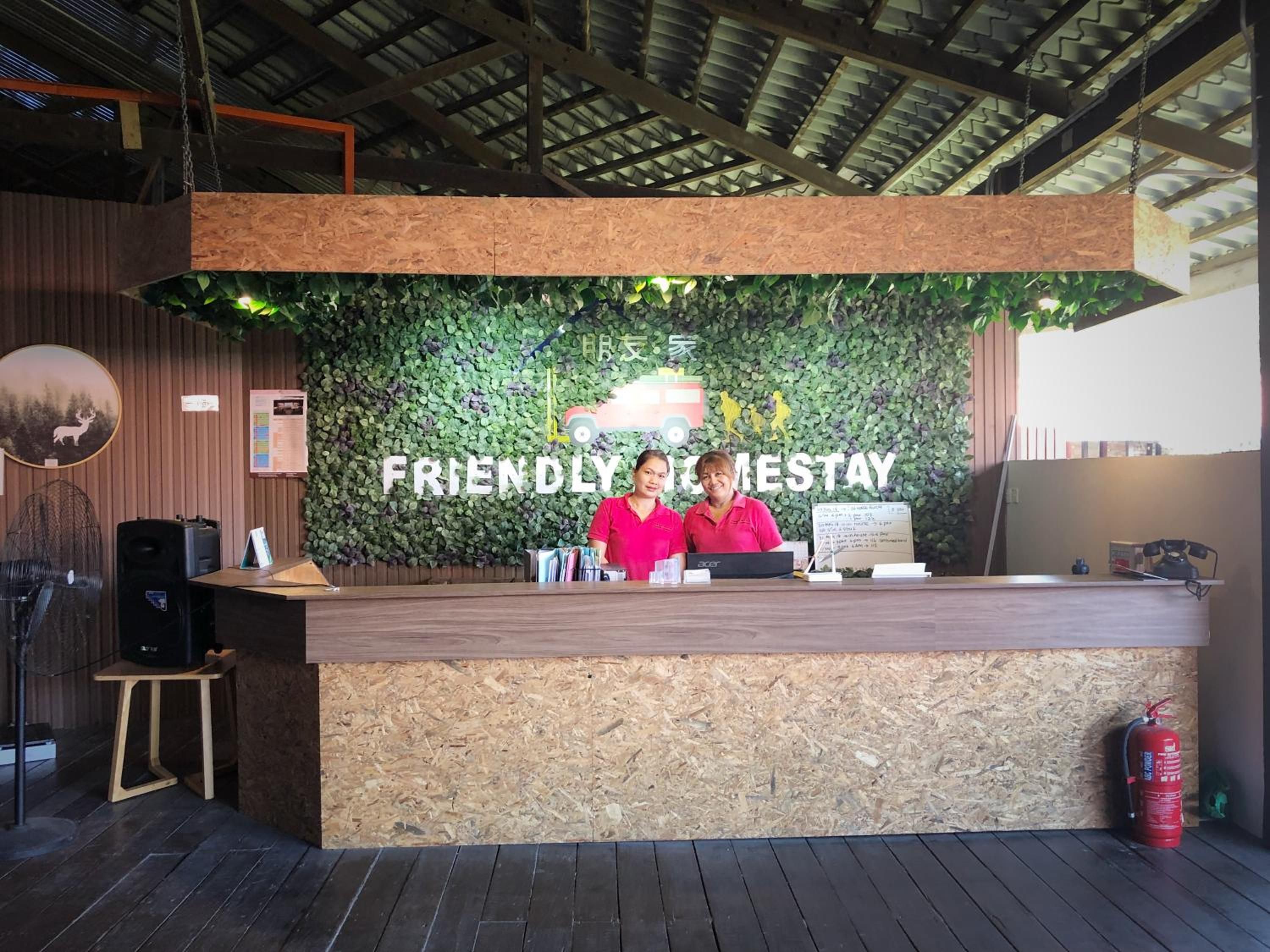 A reception desk with a green leafy wall backdrop, two staff members in pink uniforms, and a wooden floor.