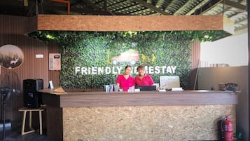 A reception desk with a green leafy wall backdrop, two staff members in pink uniforms, and a wooden floor.