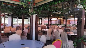 An indoor dining area with tables and chairs, covered by a roof with greenery.