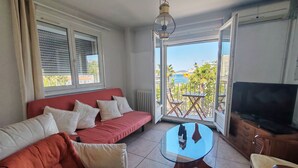 Una sala de estar con un sofá rojo, una mesa de centro de vidrio, un televisor y un balcón con vista al mar.