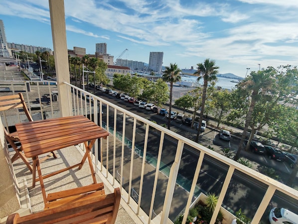 Ein Balkon mit einer Holzbank und -brüstung, der auf einen Parkplatz mit Autos und Palmen blickt.