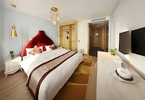 Ein Hotelzimmer mit einem großen Bett, einem Schreibtisch, einem Flachbildfernseher, einem Kleiderschrank und einem Spiegel.