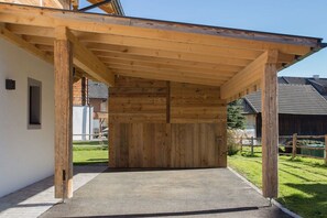 Ein überdachter Außenbereich mit Betonboden, Holzbalken und einer weißen Wand.