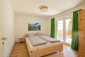 Ein Schlafzimmer mit einem hölzernen Bett, einem Nachttisch, einem Gemälde und einer Glaswand zum Außenbereich.