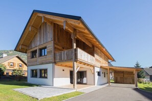 Ein zweistöckiges Holzhaus mit Balkon und überdachter Auffahrt, bewölkter Himmel.