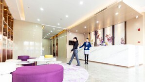 Eine moderne Lobby mit einer Rezeption, Sitzbereichen und einem großen violetten Hocker.